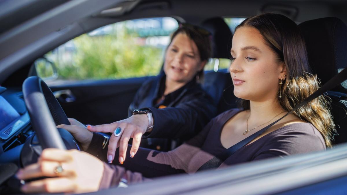 A young driver sits in the front seat of a car while the driving instructor next to them gives guidance.