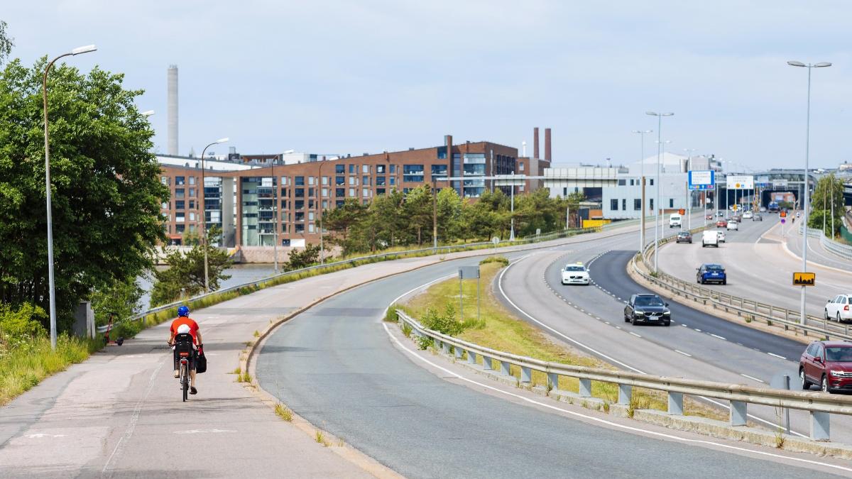 Pyöräilijä pyöräilee pyörätiellä Itäväylällä Helsingissä, kuvassa näkyy myös autoja ajamassa Itäväylällä