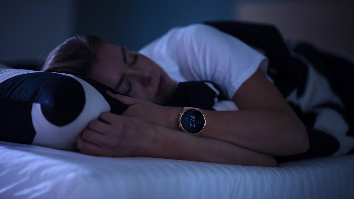 A woman is sleeping in black-and-white sheets with a smartwatch on her wrist.