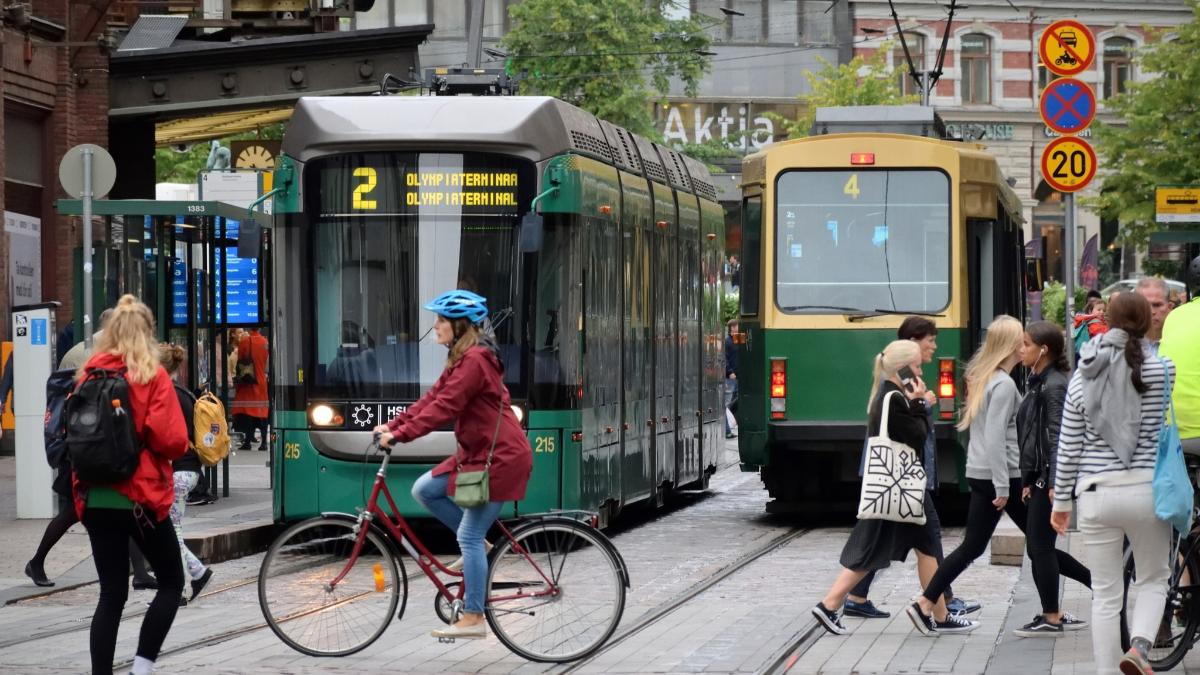 Kaksi raitiovaunua kohtaavat toisensa Helsingissä, kuvan etuosassa pyöräilijä ja useita kävelijöitä ylittämässä tietä