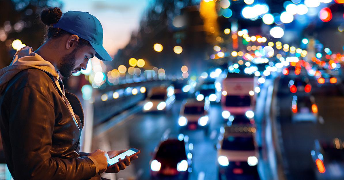 Mies käyttää älypuhelinta, taustalla liikennettä (Kuva: Shutterstock)