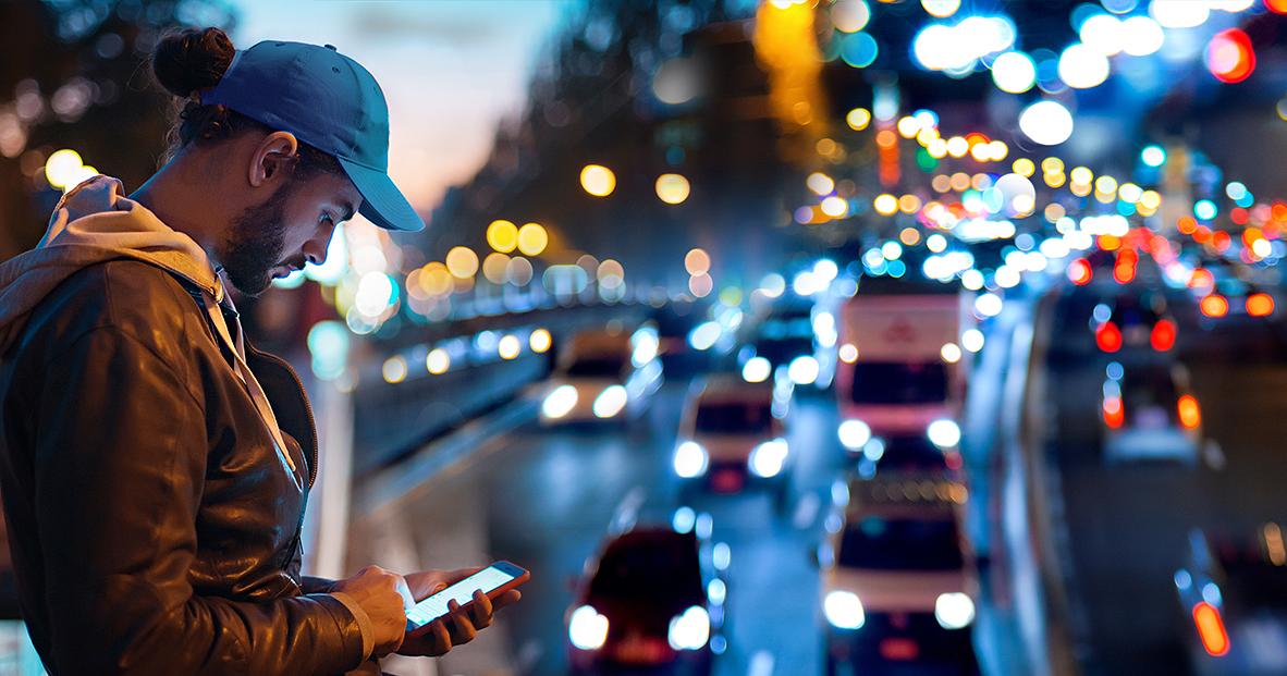Ung man använder mobil telefon, på bakgrund trafik och bilarnas ljus (Bild: KM)