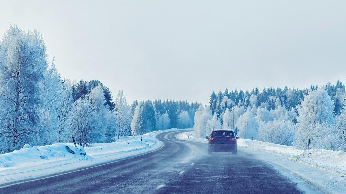Auto avaa maantielle talvella, puut ovat lumen peitossa