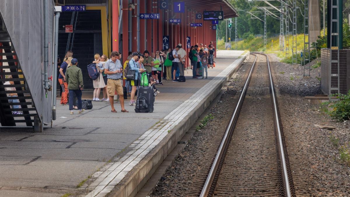 Kuvassa oikealla näkyy raide ja vasemmalla asemarakennus ja joukko ihmisiä odottamassa junaa