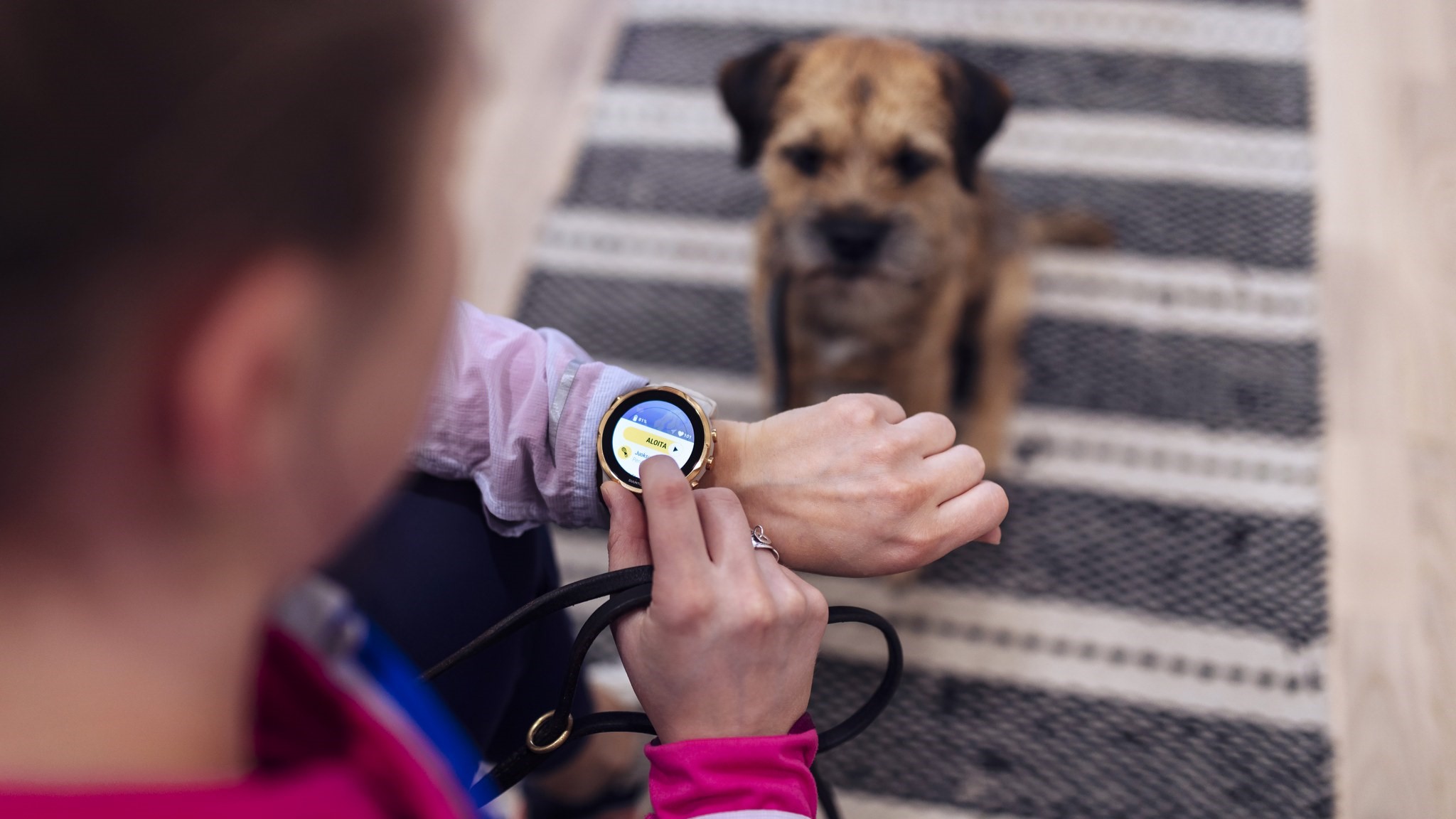 En kvinna ska gå ut på promenad med sin hund och tittar på sin smartklocka. (Bild: Mika Pakarinen, Keksi/LVM)